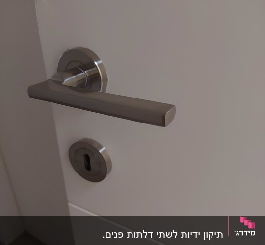 ידית דלת מתכתית ומנעול על דלת לבנה